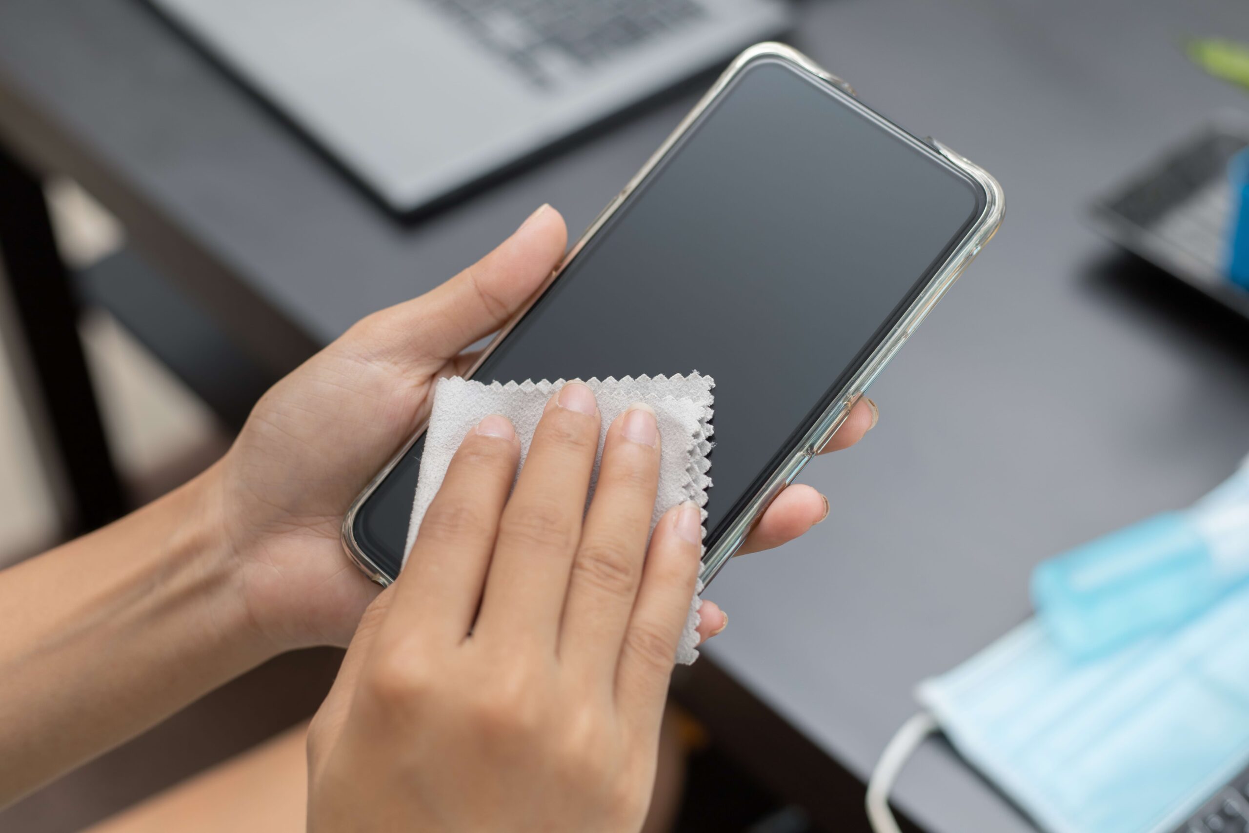 Mulher limpando a tela de um celular com um pano e álcool