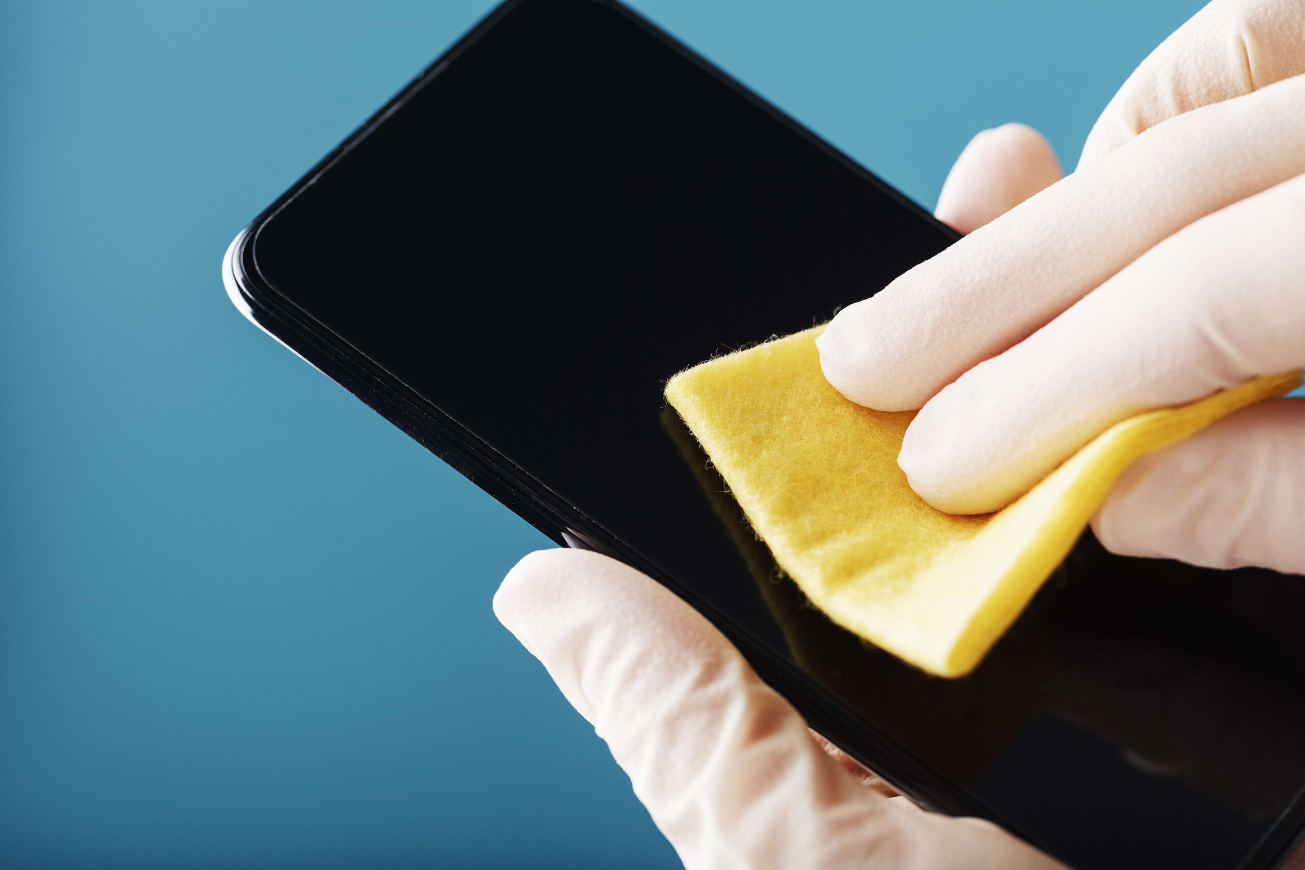 Pessoa com luva branca limpando a tela do celular com flanela amarela