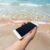 Mão segurando um iphone na praia em frente ao mar