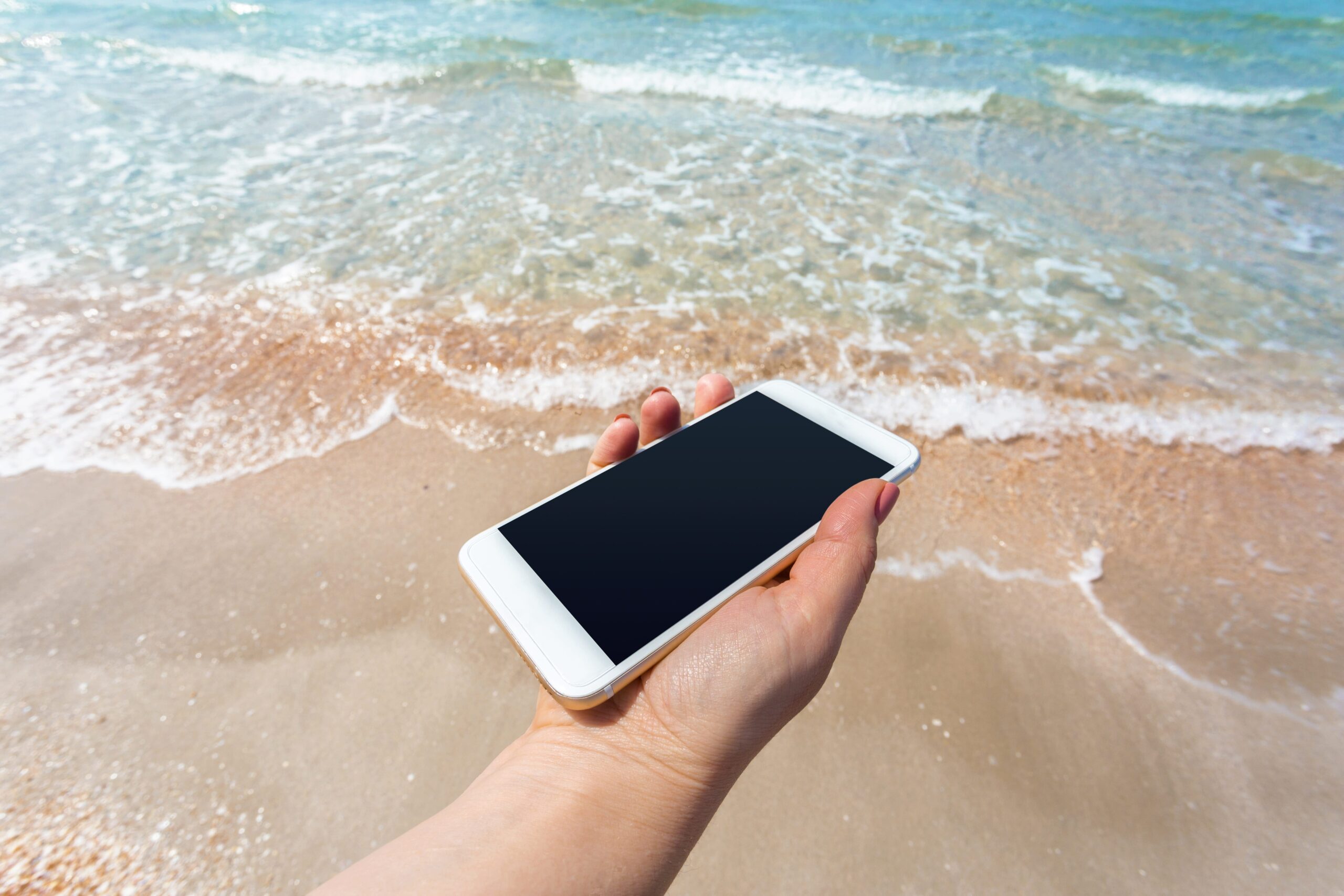 Mão segurando um iphone na praia em frente ao mar