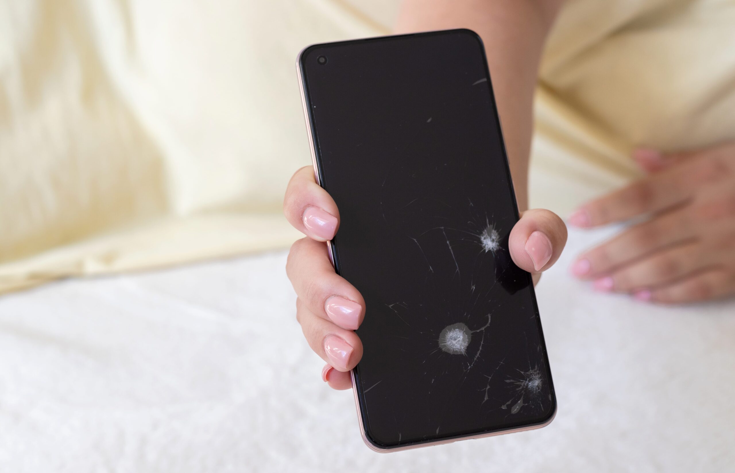 Mão segurando um celular preto com a tela quebrada e rachada