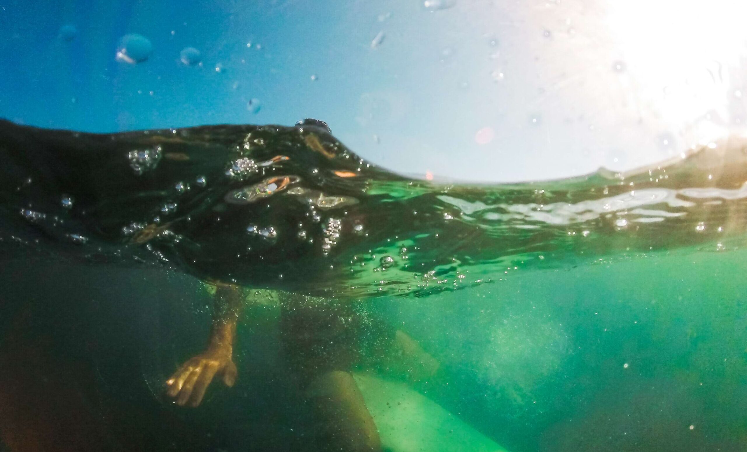 Homem sentado em prancha debaixo d'água no mar