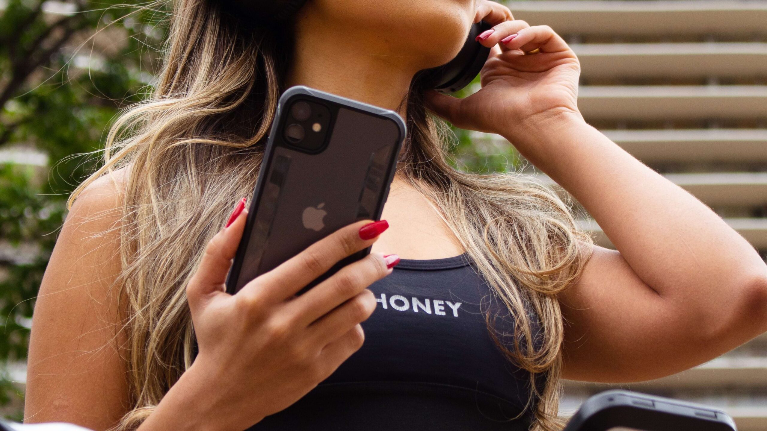 Mulher segurando iPhone com capa da GShield e ajustando fone de ouvido