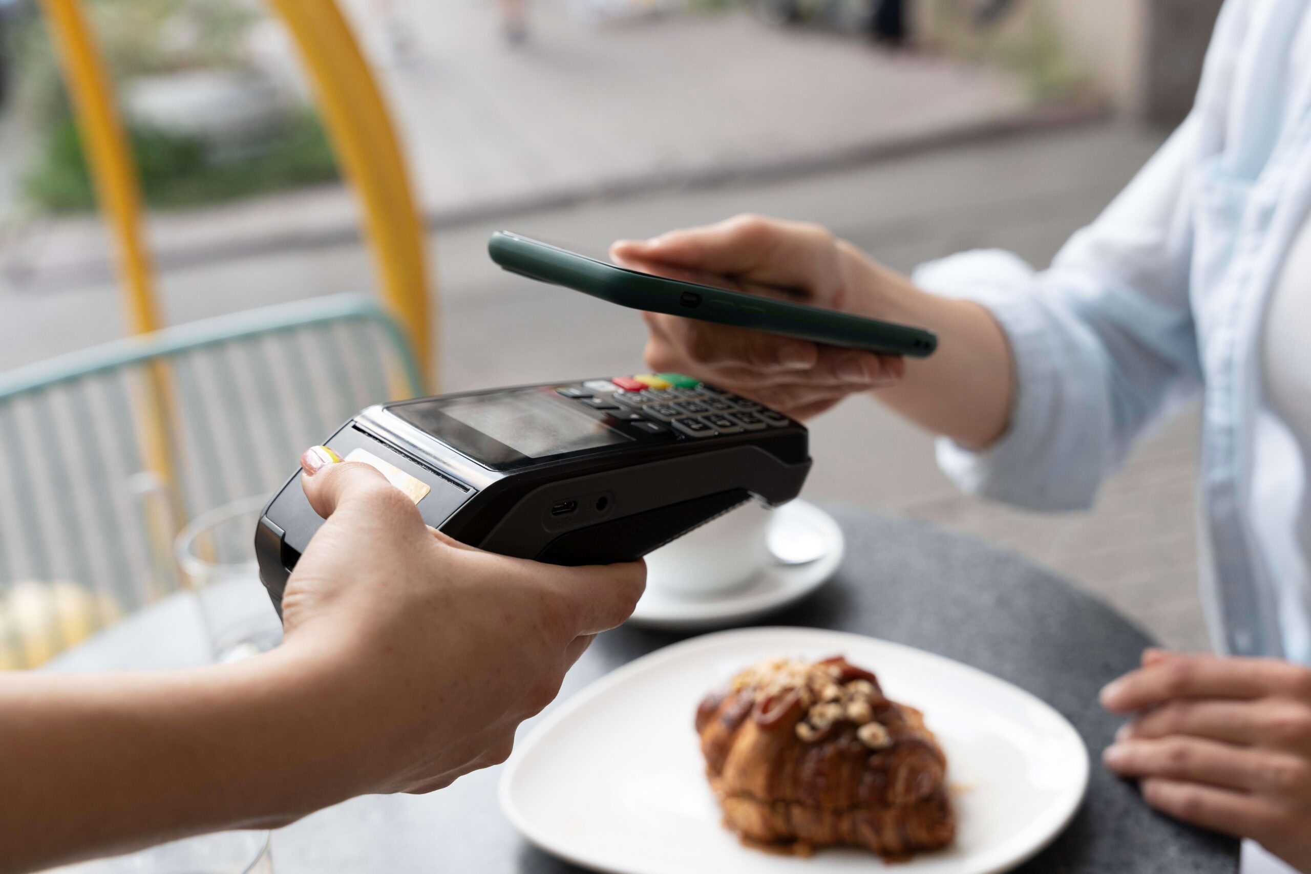 Pessoa colocando smartphone próximo a uma máquina de cartão de crédito utilizando tecnologia NFC de aproximação