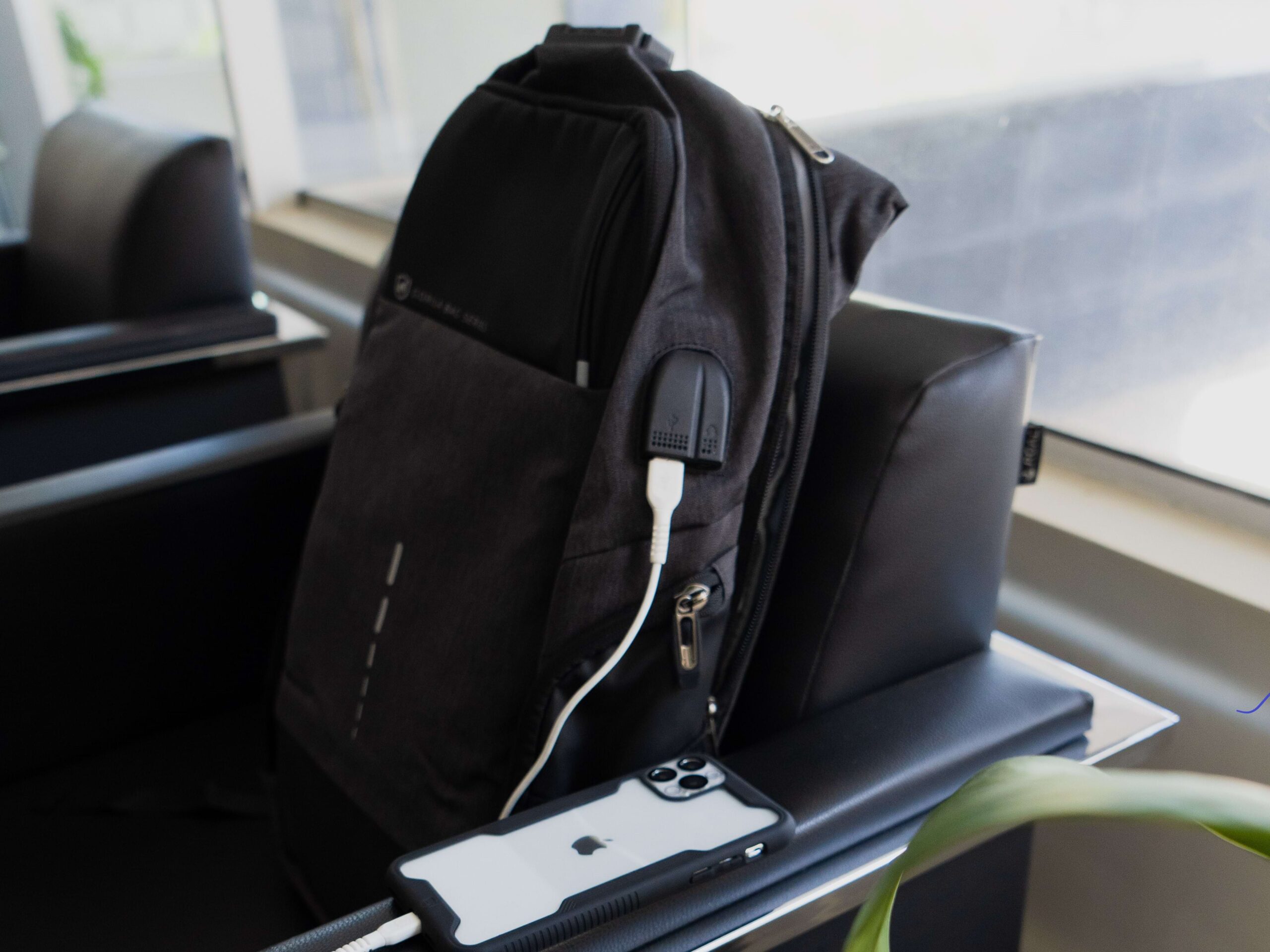 Mochila antifurto da GShield em cima de cadeira no aeroporto ao lado de iPhone branco com capa preta e transparente