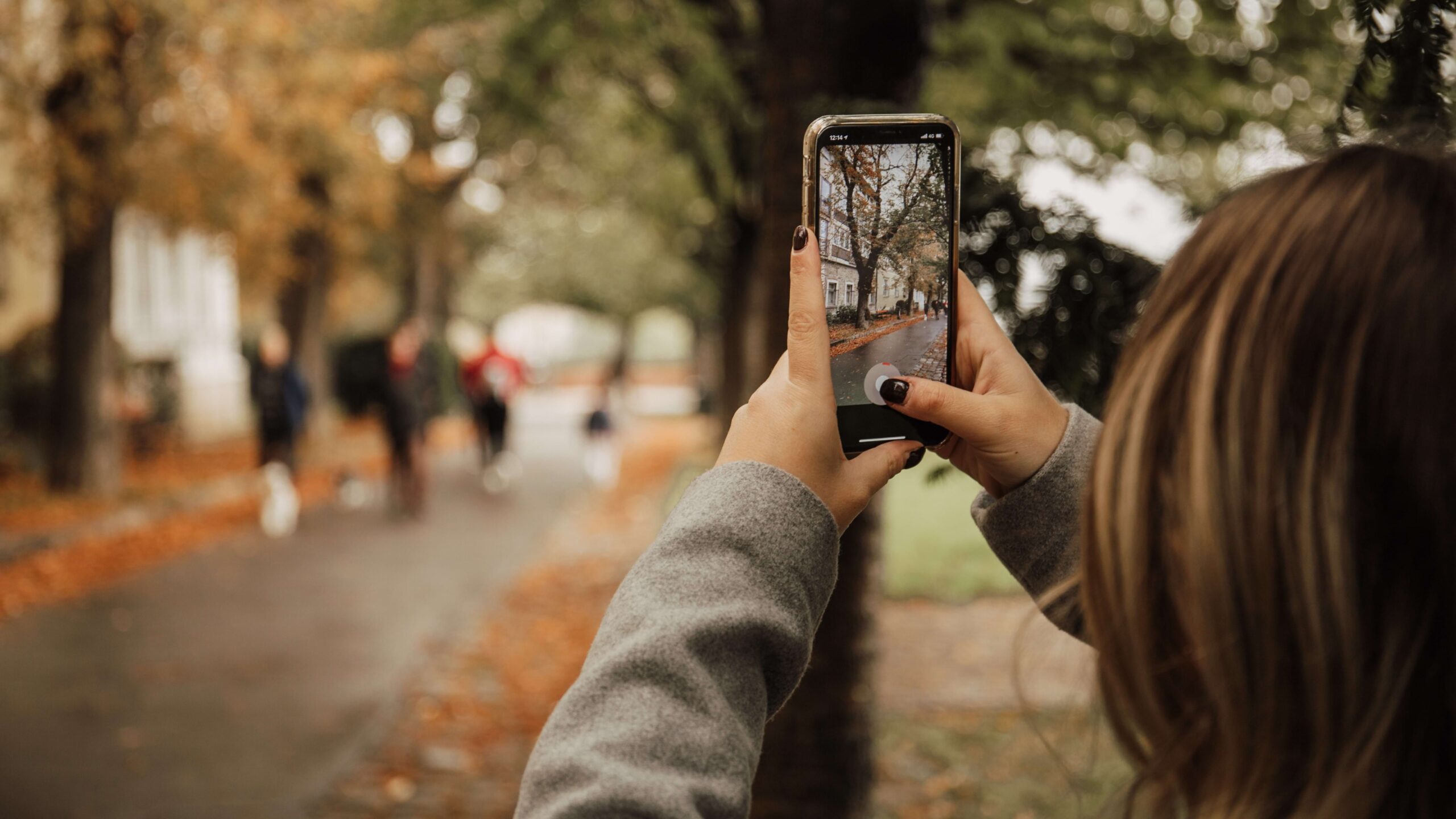 Mulher tirando foto de uma rua com folhas de orvalho caídas no chão, com iPhone
