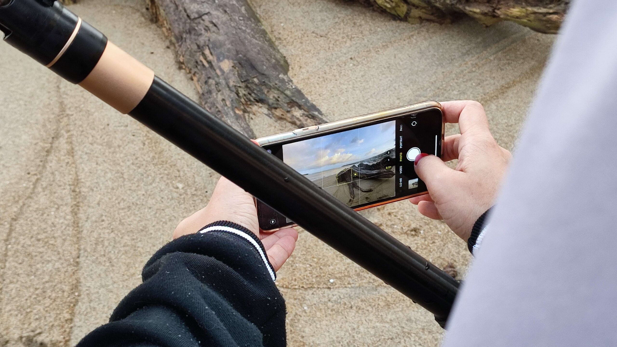Pessoa tirando foto de paisagem com celular Xiaomi, vestindo uma blusa preta de manga longa e segurando um bastão