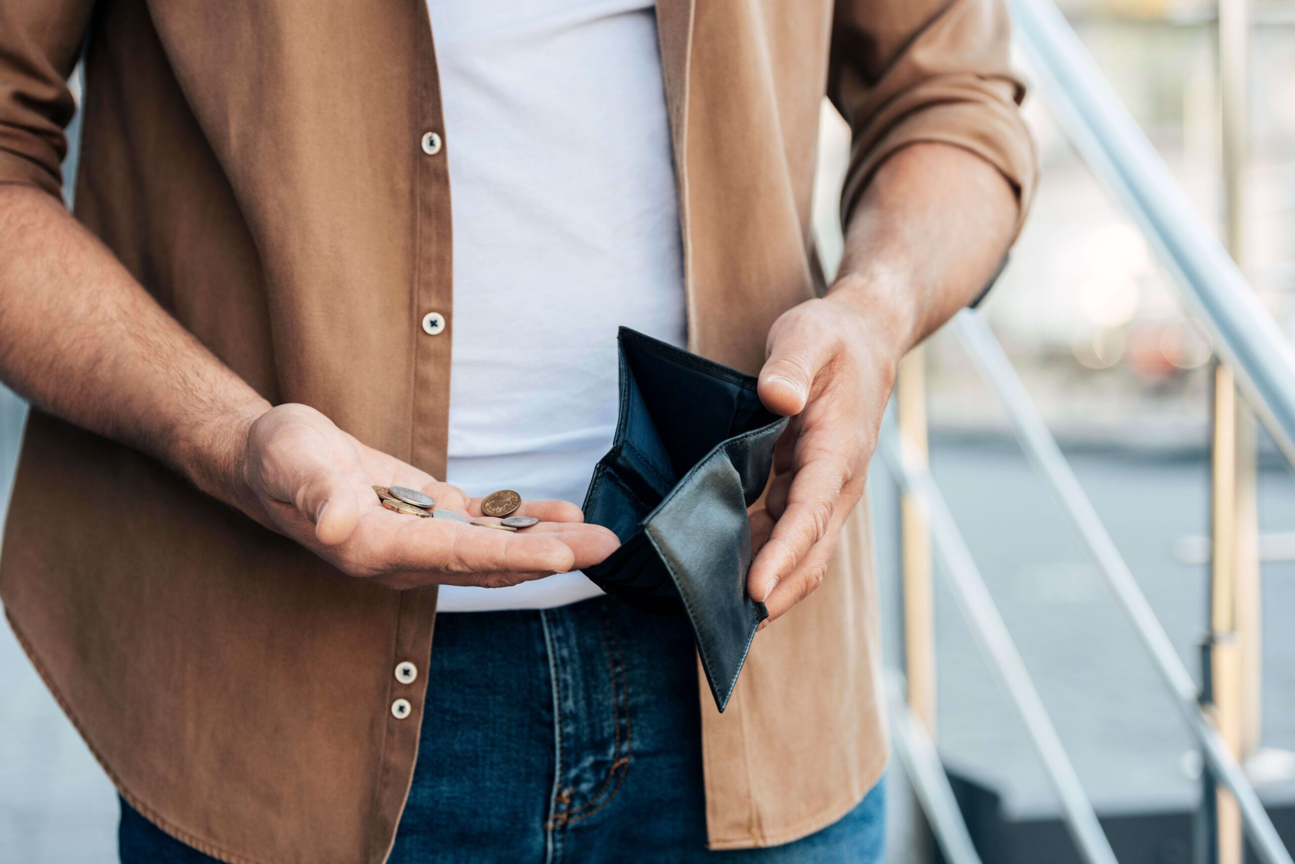 Homem de blusa branca e jaqueta marrom, colocando dinheiro em uma carteira de couro preta